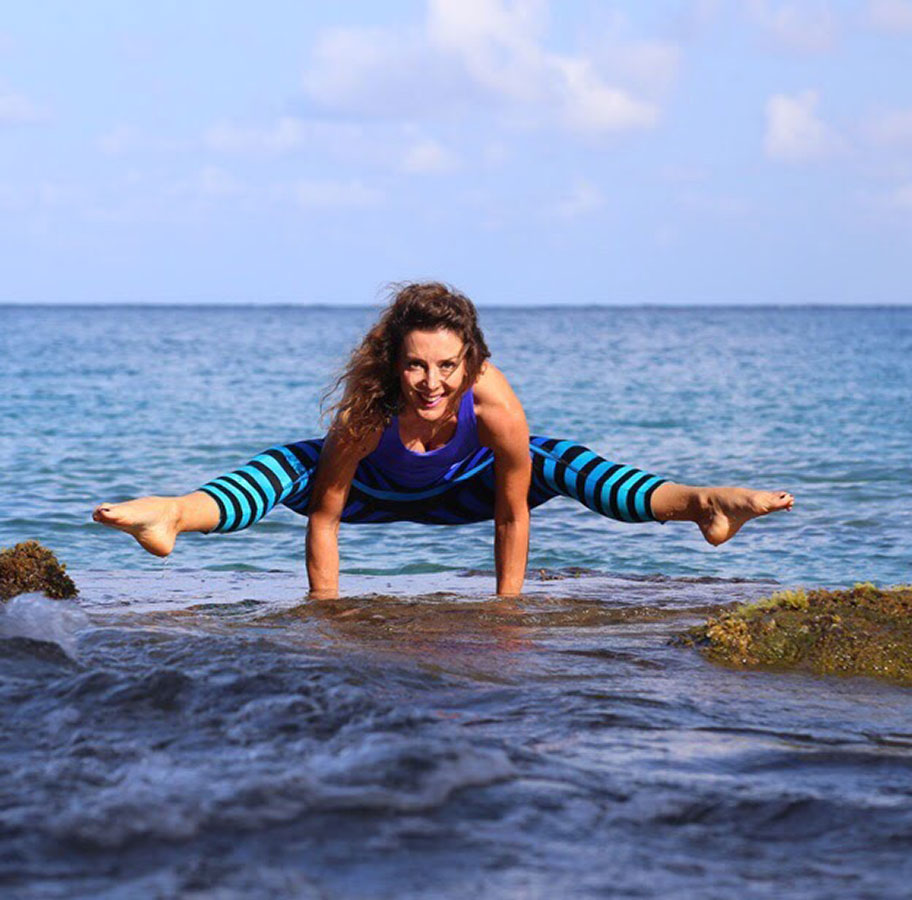 wOMAN PERFORMING A yOGA pose on rocks by the sea